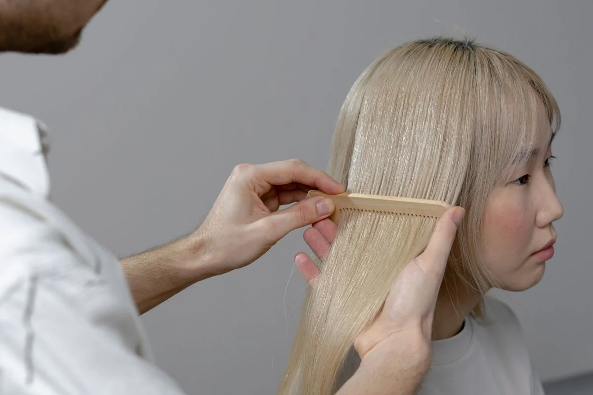 Hairstylist combing a client’s long blonde hair in the salon