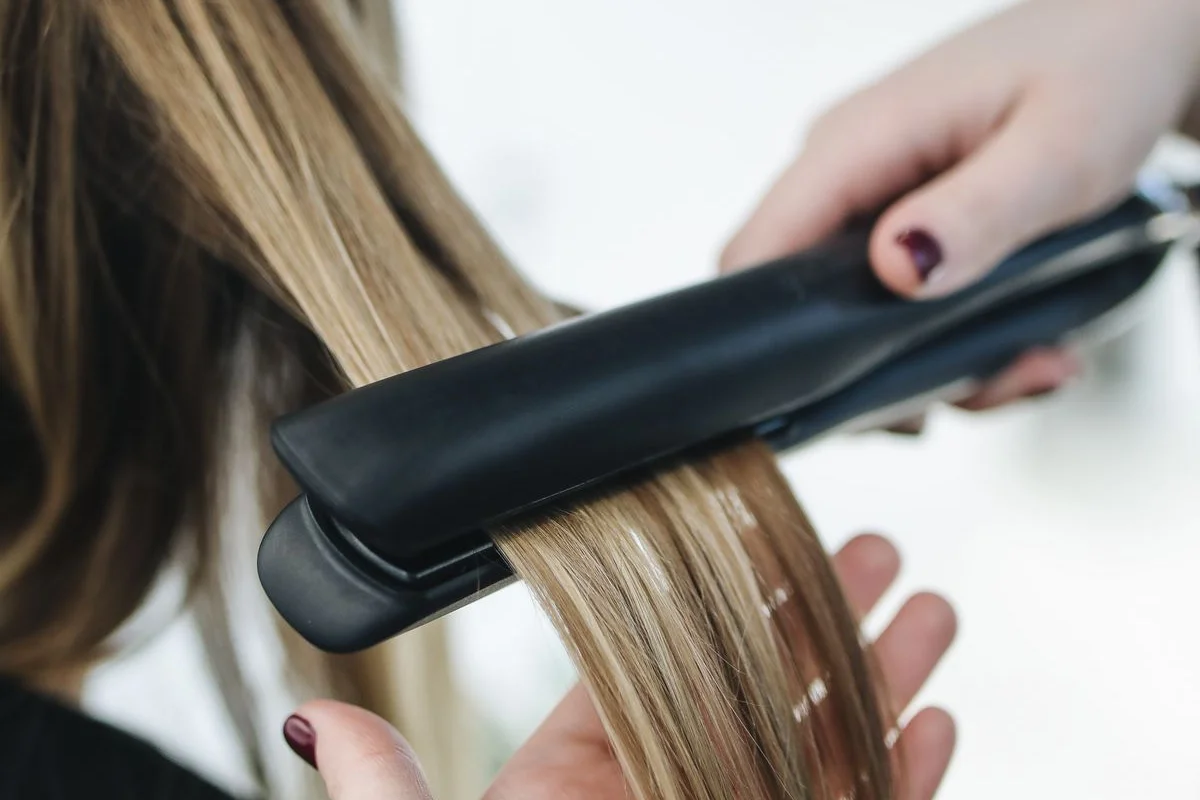 Hairstylist sealing a strand of blonde hair with a flat iron