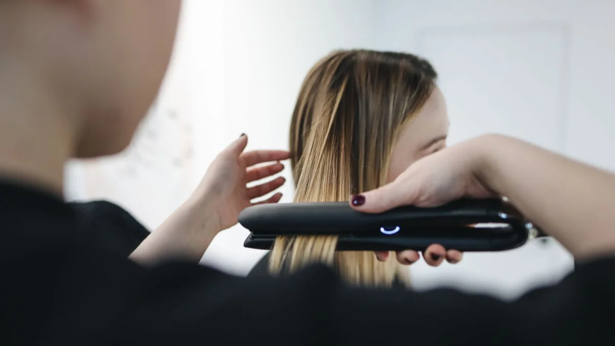 Stylist straightening a client’s hair with a flat iron